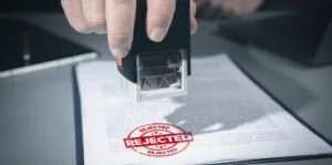 stamp-rejected-rejected-red-stamp-official-documcent-documents-reviewedreject-investment-projects-banned-denied-declined-negative-stamp-concept-1-1-scaled-scaled | V.Valenzuela Law | V.Valenzuela Law Person stamping a document with a red 'REJECTED' stamp visible on the page underneath.
