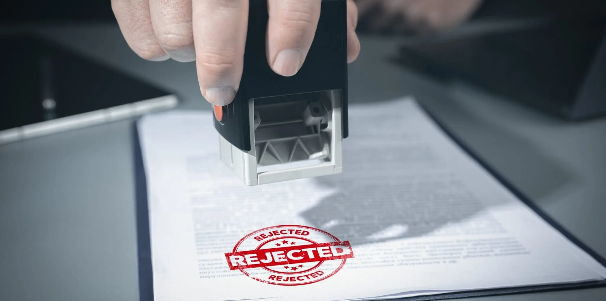 Person stamping a document with a red 'REJECTED' stamp visible on the page underneath.