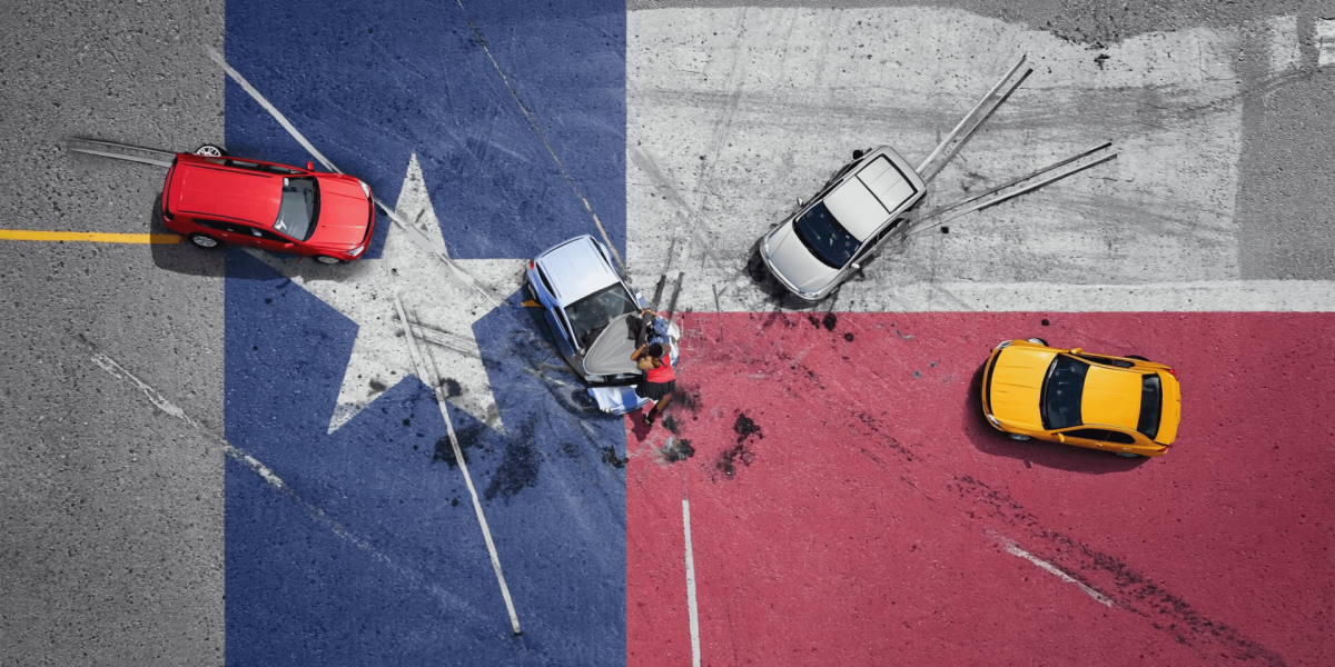 Aerial view of a multi-car crash on a color-blocked road, with a red car on the left, a blue car center, a white car nearby, and a yellow car on the red section; two people stand near the blue car amid scattered debris.